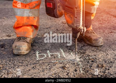 Nahaufnahme eines Bauherstellers, der mit einem Akku-Bohrhammer Löcher in der Straße an der vom Bauingenieur gekennzeichneten Stelle bohrt Stockfoto