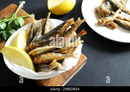 Leckere gebratene Sardinen mit Zitrone in einer weißen Schüssel auf grauem Hintergrund. Draufsicht. Kopierbereich. Stockfoto