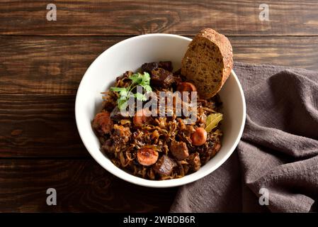 Gedünsteter Kohl (polnische Bigos) mit Sauerkraut, Pilzen, Räucherfleisch und Gewürzen in einer weißen Schüssel auf rustikalem Holztisch. Nahansicht Stockfoto