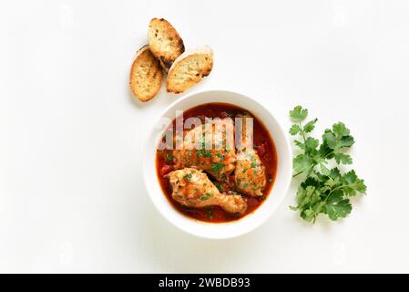 Hühnereintopf mit Tomaten und Kräutern in der Schüssel, Korianderblättern und geröstetem Brot auf weißem Hintergrund mit Kopierraum. Auflauf mit Hühnchen und Tomaten. T Stockfoto