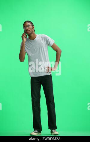 Ein Mann in einem grauen T-Shirt, auf grünem Hintergrund, mit einem Telefon Stockfoto