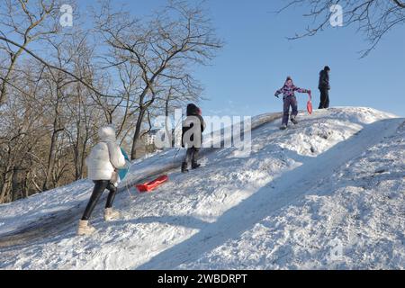 ODESA, UKRAINE - 10. JANUAR 2024 - Kinder fahren bergauf, während sie im Premohy (Victory) Park in Odesa, Süd-Ukraine, Schlittenfahren genießen. Stockfoto