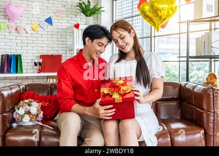 Aufgeregte junge asiatische Frau, die eine Geschenkbox öffnet und ein gutes unerwartetes Geschenk vom Ehemann zu Hause erhält, liebevoller Freund, der eine romantische Überraschung macht Stockfoto