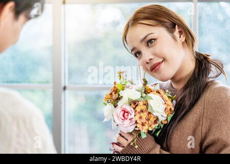 Asiatischer junger Mann überrascht seine schöne Freundin mit Blumenstrauß zu Hause, attraktives romantisches neues Ehepaar männlich und weiblich Stockfoto