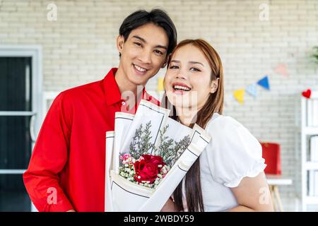 Eine junge asiatische Frau erhält einen Blumenstrauß roter Rosen als Geschenk von einem Mann oder Freund, Valentinstag. Stockfoto