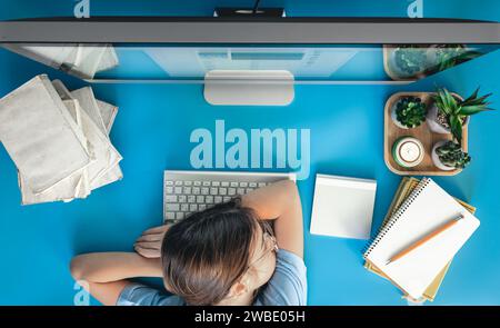 Ein müdes Mädchen liegt auf einem Tisch vor einem Computer mit Notizblöcken und Büchern. Stockfoto