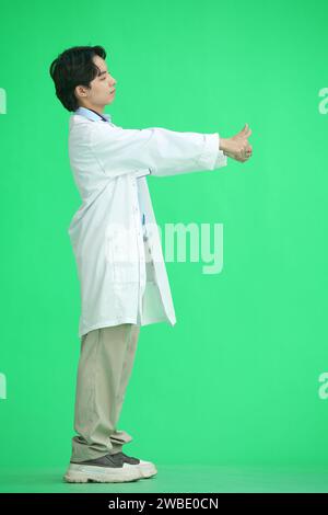 Der Doktor auf grünem Hintergrund, in voller Höhe, zeigt seine Daumen nach oben Stockfoto