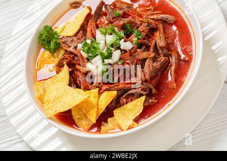 Birria de Res, mexikanischer Rindereintopf in heißer Paprikasauce mit roher Zwiebeln und gehacktem Koriander, Taco-Chips in weißer Schüssel, Nahaufnahme, niederländischer Angelleig Stockfoto