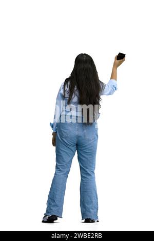 Ein Mädchen in einem blauen Hemd, auf weißem Hintergrund, in voller Höhe, mit dem Handy winkend, Rückansicht Stockfoto