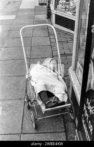 Ein Kleinkind, das in einem Kinderwagen vor Souch's Zeitungskiosk, Tobacconist & Post Office, Lordship Lane, Tottenham, London, gelassen wurde - Mittwoch, den 8. Januar 1969 Stockfoto