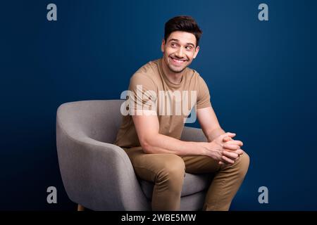 Foto des funky optimistischen fröhlichen Mannes gekleidet beige T-Shirt sitzen im Sessel Blick auf Verkauf leeren Raum isoliert auf blauem Hintergrund Stockfoto