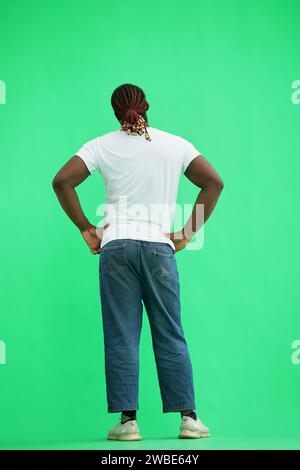 Ein Mann in einem weißen T-Shirt auf grünem Hintergrund hält seine Hände an seinem Gürtel, Rückansicht Stockfoto