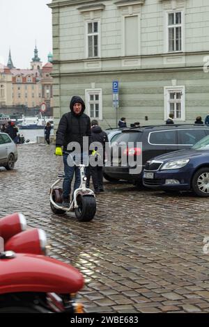 Foto eines Mannes, der einen Elektroroller in den Straßen von Prag fährt, während er im Winter schneit Stockfoto