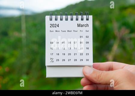 Hand hält März 2024 weißen Kalender mit Naturhintergrund. Feiertags- und Kalenderkonzept. Stockfoto