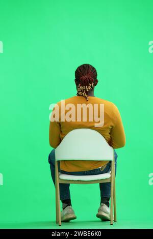 Ein Mann in einem gelben Pullover auf grünem Hintergrund sitzt auf einem Stuhl und schaut zur Seite, nach hinten Stockfoto