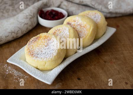 Teller mit leckeren Hüttenkäse-Pfannkuchen mit Marmelade auf hölzernem Hintergrund. Syrniky. Traditionelles ukrainisches Frühstück Stockfoto