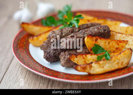 Lula Kebabs auf einem weißen Teller mit rotem Rand mit gebackenen Kartoffeln und Grünzeug. Lamb Lula Kebab, Rindfleisch lula Kebab, Hühnchen lula Kebab Nahaufnahme. Stockfoto