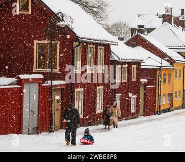 Ein Mann sah, wie er sein Kind auf einem Schlitten im Zentrum Stockholms während eines Schneesturms zerrte. Rote historische Häuser in der Nähe des Nytorg-Platzes. Kalter Wintertag. Stockfoto