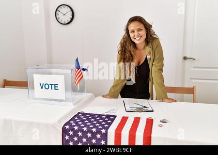 Junge, wunderschöne hispanische Frau, Wahlpräsidentin, die selbstbewusst am Wahlkollegium lächelt Stockfoto