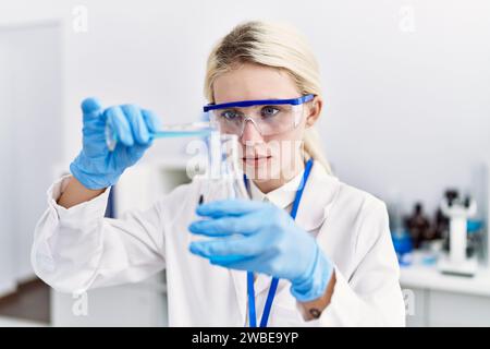 Junge blonde Wissenschaftlerin, die im Labor Flüssigkeit auf das Reagenzglas gießt Stockfoto