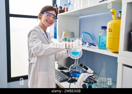 Junge blonde Wissenschaftlerin, die im Labor Flüssigkeit auf das Reagenzglas gießt Stockfoto
