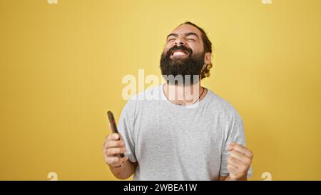 Fröhlicher bärtiger Mann lacht mit Kamm isoliert auf gelbem Hintergrund Stockfoto
