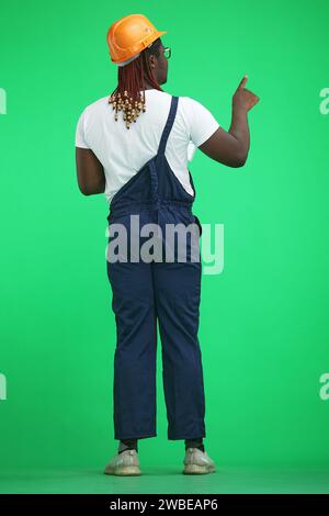 Ein Mann in Arbeitsuniform, auf grünem Hintergrund, in voller Höhe, zeigt zur Seite, nach hinten Stockfoto