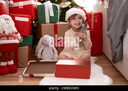 Ein entzückendes Mädchen, das zu Hause am weihnachtsbaum sitzt Stockfoto