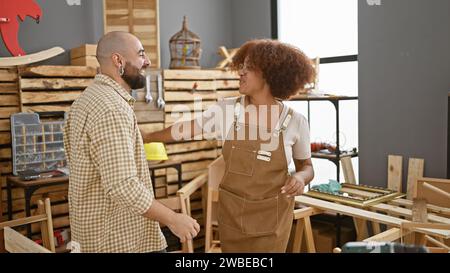 Lächelnde Zimmerleute, Mann und Frau, tanzt selbstbewusst zur Musik im Herzen ihrer Tischlerei, um ihren Beruf und den Rhythmus von zu genießen Stockfoto