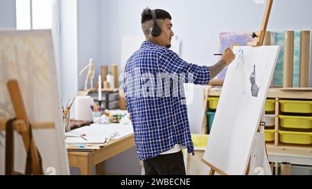 Porträt eines tätowierten jungen lateinmannes, ein Künstler, der in seine Zeichnung vertieft ist und in seinem Kunststudio inspirierende Audiosignale über Kopfhörer hört Stockfoto