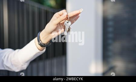 Nahaufnahme der Hand einer Frau, die Hausschlüssel in einer sonnigen Straße hält. Stockfoto