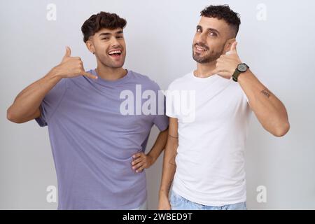 Homosexuelles schwules Paar, das über weißem Hintergrund steht und lächelnd mit Hand und Fingern telefoniert, als würde man am Telefon sprechen. Kommunizierende Co Stockfoto