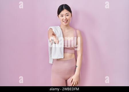 Chinesische junge Frau in Sportbekleidung und Handtuch lächelnd und freundlich mit Handballenhand, die Hilfe und Akzeptanz gibt. Stockfoto