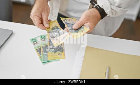 Gutaussehender kaukasischer Geschäftsmann mittleren Alters, der Stapel australischer Dollar im Amt zählt und Investitionserfolg in Schwung nimmt Stockfoto