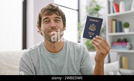 Ein glücklicher junger Mann, der zu Hause auf seinem Sofa sitzt, grinst von Ohr zu Ohr und stellt seinen Pass der vereinigten staaten zur Schau. Dieses selbstbewusste, bärtige, blonde Erwachsene ich Stockfoto