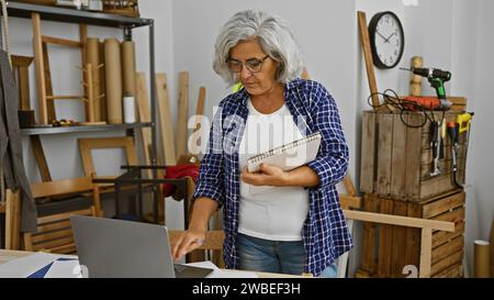 Eine reife Frau prüft Pläne in einer Holzwerkstatt, umgeben von Werkzeugen und Holz Stockfoto