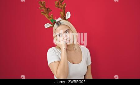 Junge schöne hispanische Frau mit Rentier-weihnachtsmütze mit Zweifelausdruck über isoliertem roten Hintergrund Stockfoto