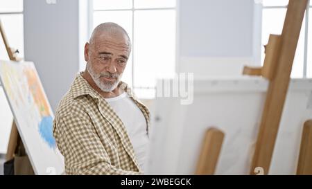 Reifer bärtiger Mann malte auf Leinwand in hellem Kunststudio Stockfoto