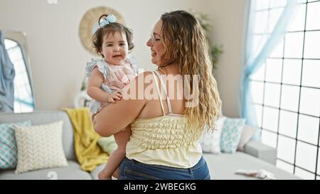 Glückliche Mutter steht zuversichtlich zu Hause, hält ihre liebenswerte Tochter in den Armen und genießt gemeinsam die Liebe der Familie in ihrem Wohnzimmer mit einem Stockfoto