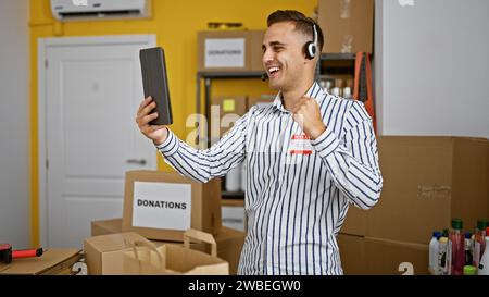 Ein fröhlicher junger Mann, der ein Headset trägt, feiert mit einer Faustpumpe in einem Lagerhaus voller Spendenboxen. Stockfoto