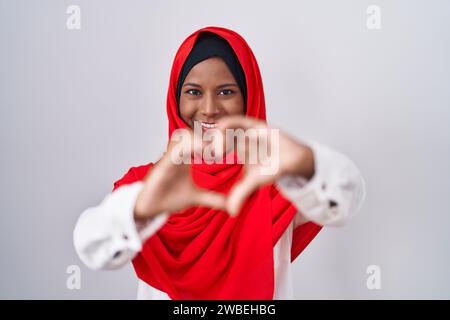 Junge arabische Frau mit traditionellem islamischem Hijab-Schal lächelt in Liebe und macht mit den Händen die Form eines Herzsymbols. Romantisches Konzept. Stockfoto