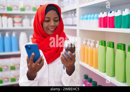 Junge schöne Frau Apotheker mit Smartphone hält Medikamentenflasche in der Apotheke Stockfoto