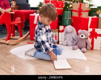 Entzückender hispanischer Junge, der den weihnachtsmann-Brief schreibt, der zu Hause am weihnachtsbaum sitzt Stockfoto