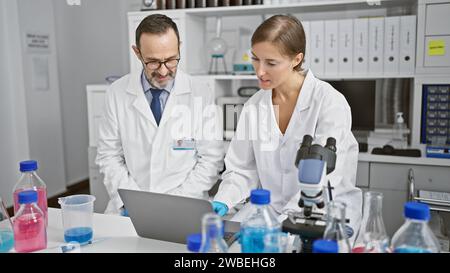 Zwei ernsthafte Wissenschaftler in Brille, vertieft in ein lebenswichtiges Forschungsgespräch über einen Laptop, die leidenschaftlich die neuesten medizinischen Erkenntnisse in ihrem sezieren Stockfoto