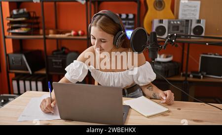 Eine junge Radioreporterin, die im Radio-Studio mit Laptop auf Papier schreibt Stockfoto