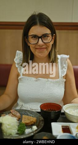 Porträt der brünetten hispanischen Frau im Restaurant, genießen ein Gourmet-Gyukatsu-Abendessen in einem modernen Café, Frau mit Gläsern und köstlichem japanischem k Stockfoto