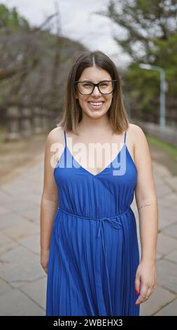 Fröhlicher Ausdruck, schöne hispanische Frau mit Brille, die Positivität und Selbstvertrauen in lässige Kleidung annimmt, während sie strahlend lächelt und zusteht Stockfoto