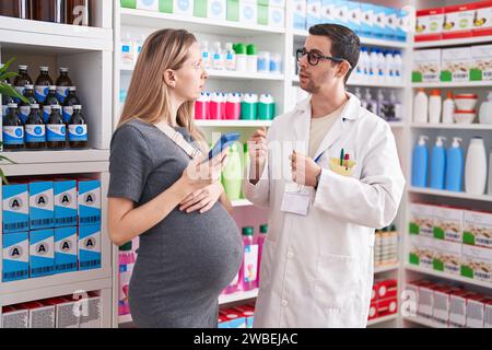 Mann und Frau, Apotheker und schwangere Klientin, die in der Apotheke ein Smartphone benutzen Stockfoto