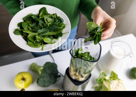 Frau gibt frischen grünen Spinat in den Mixer, um gesunden Detox Smoothie aus Gemüse und Obst in der Küche zu machen Stockfoto