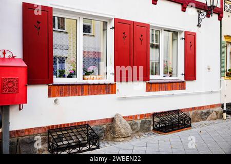 Zwei italienische Fenster an der weißen Wandfassade mit offenen roten klassischen Fensterläden und Blumen auf der Fensterbank Stockfoto